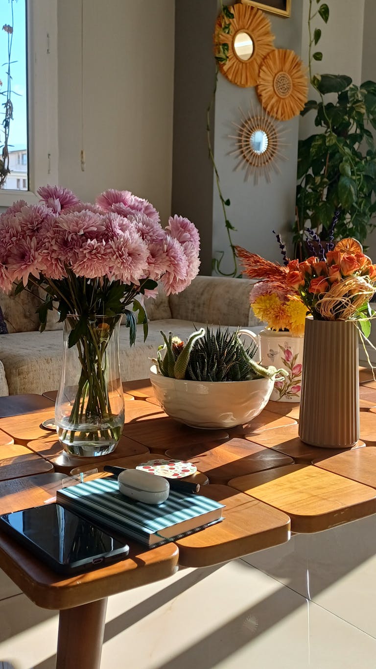 A sunlit living room features flowers, greenery, and decor, creating a cozy ambiance.