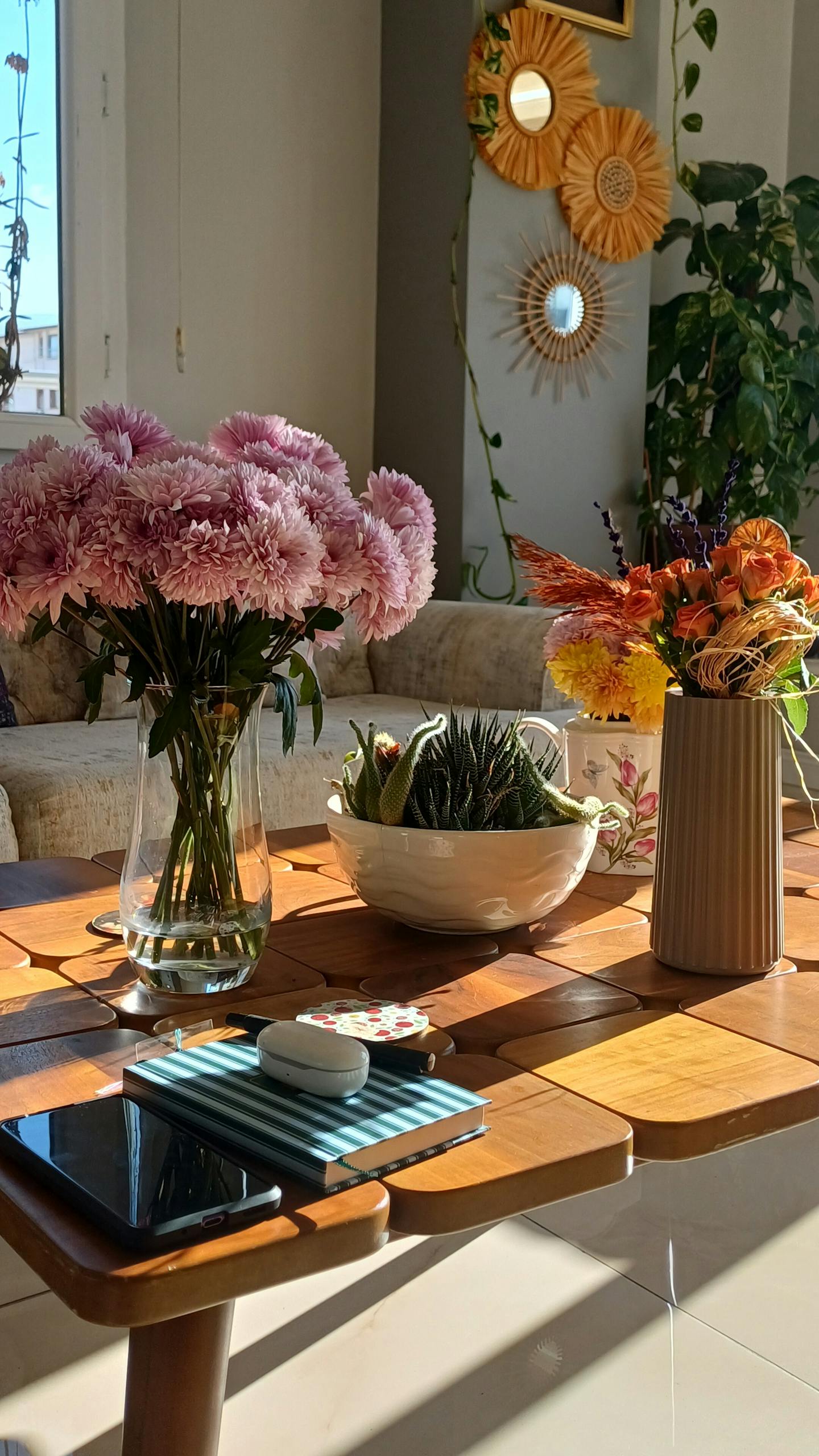A sunlit living room features flowers, greenery, and decor, creating a cozy ambiance.